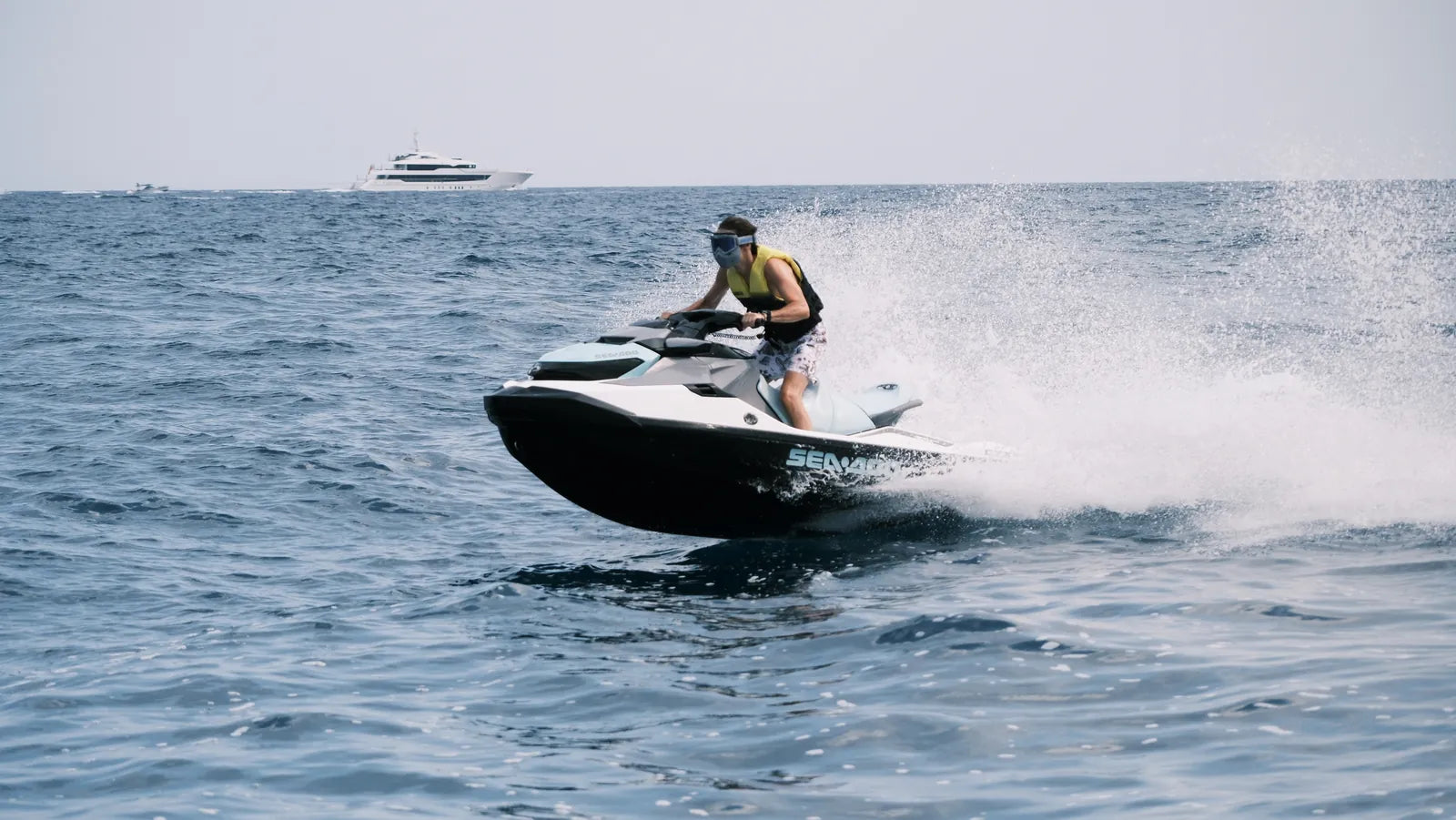 Rider on a jet ski in open sea, a yacht on the horizon